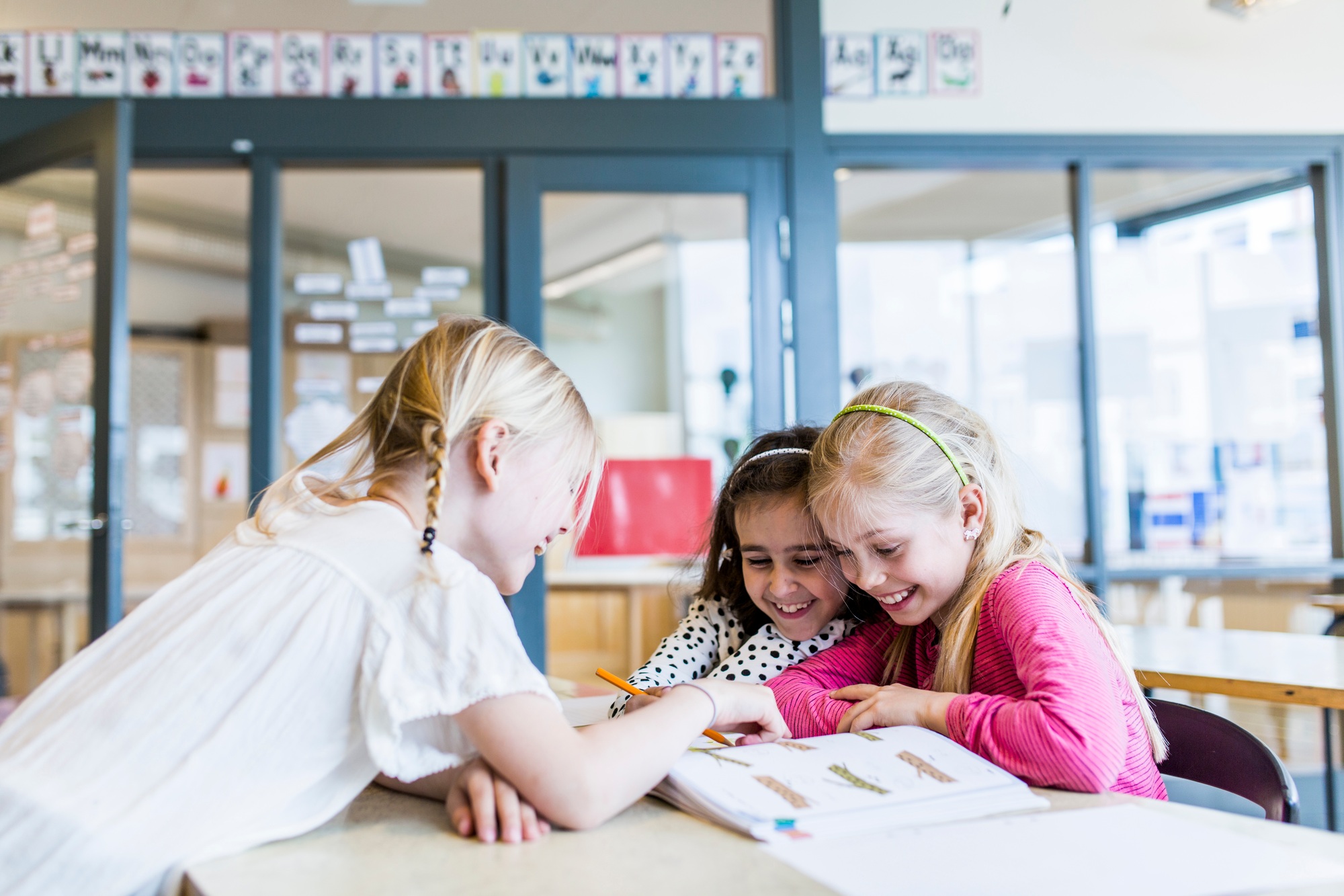 Girls (8-9) reading and laughing in classroom