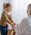 laughing child playing with wooden figurines near blurred mom at home