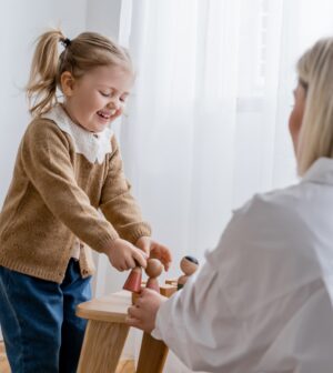 laughing child playing with wooden figurines near blurred mom at home