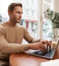 Serious looking cafe owner, handsome man working on laptop, visitor in coffee shop sending an email