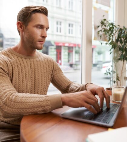 Serious looking cafe owner, handsome man working on laptop, visitor in coffee shop sending an email