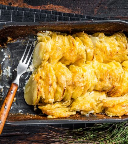 Potato casserole Gratin Dauphinois in a baking dish. Dark wooden background. Top View