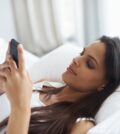 First text of the day. Shot of a beautiful young woman relaxing in bed with her mobile phone.