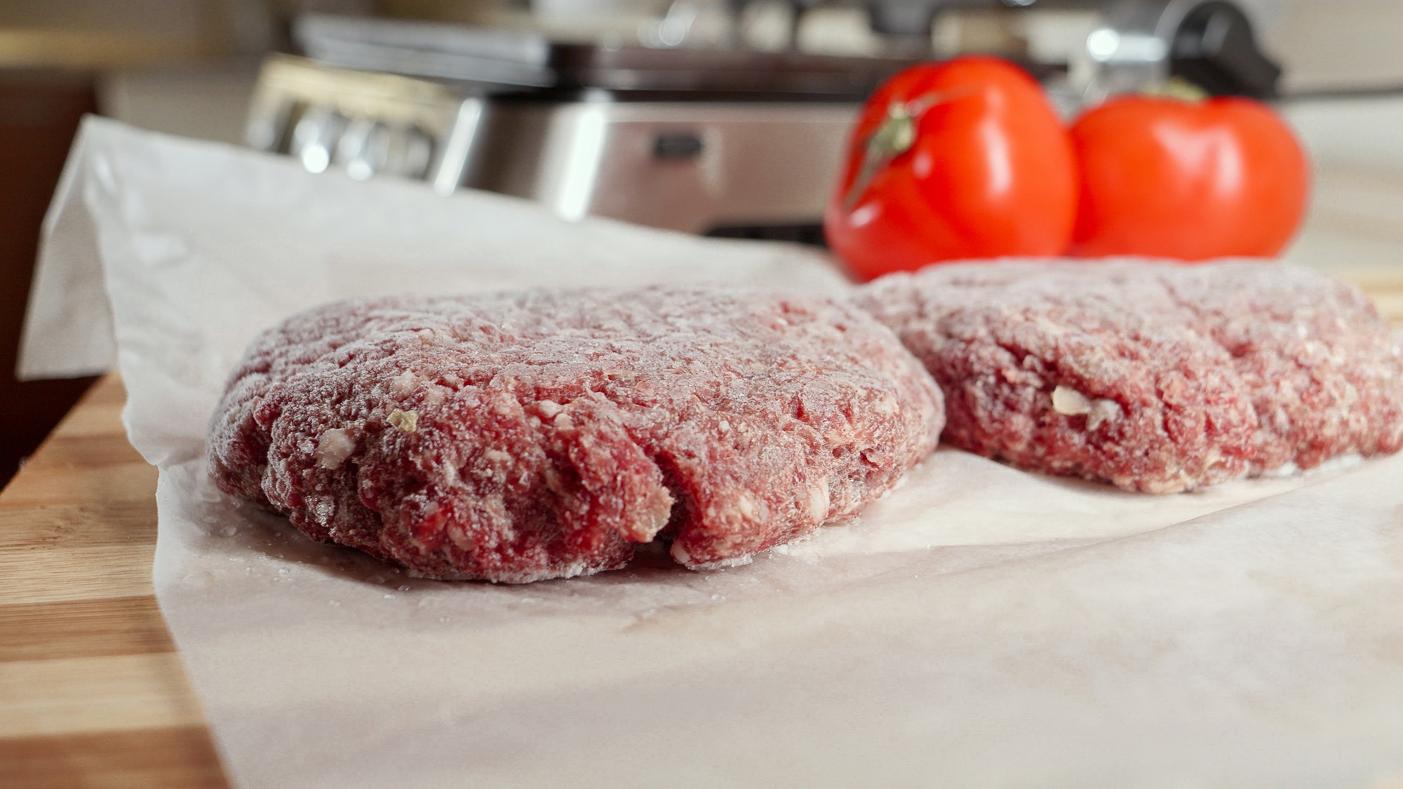 Frozen hamburger patties and ingredients lying on kitchen table next to electric grill.