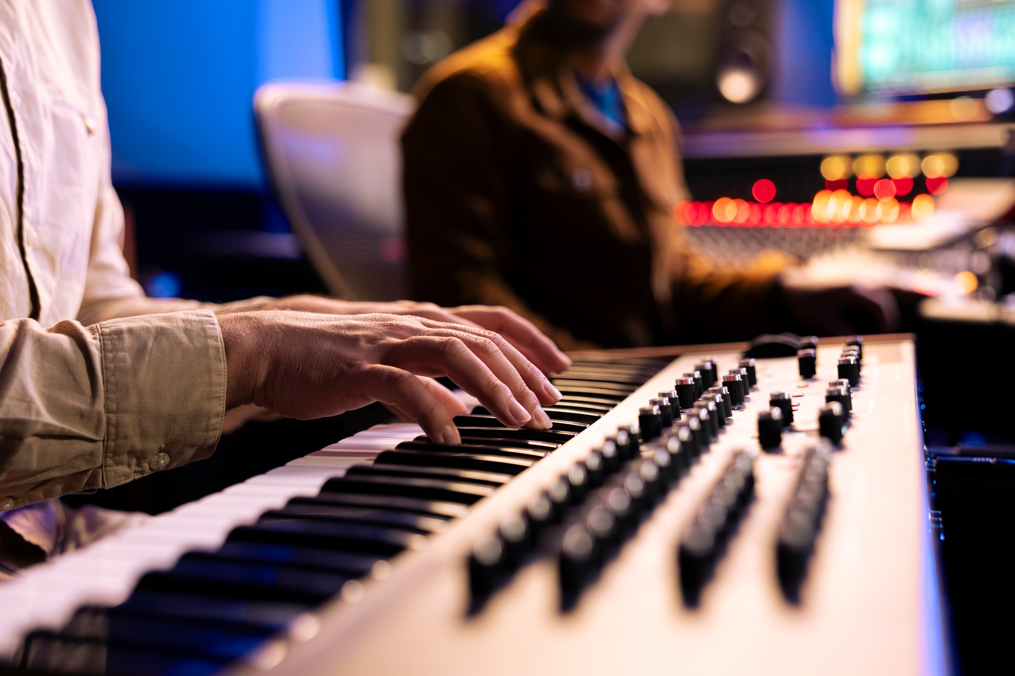 Male singer playing notes on electronic keyboard piano in music recording studio