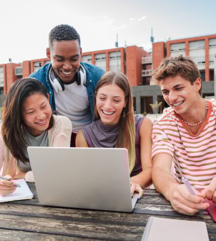 Teamwork of teenage students using a laptop to prepare a exam. Group of classmates learning together