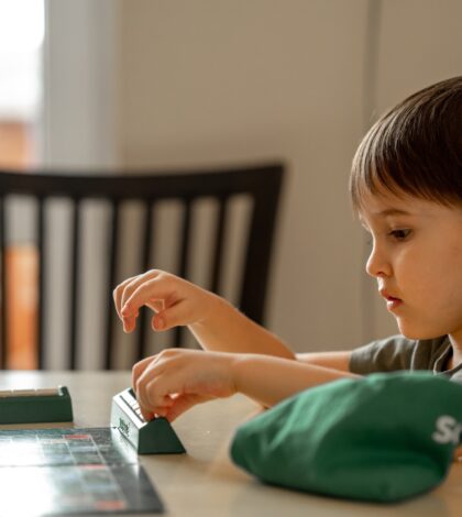 The child sits at the table and plays a board game. Playing words